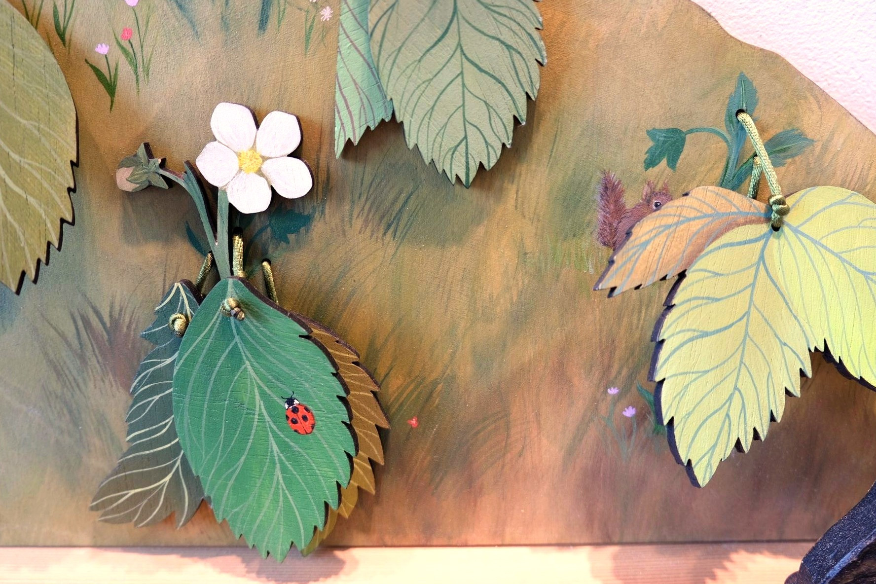 Layered painted leaves in the strawberry patch conceal details from the ladybug’s life cycle.
