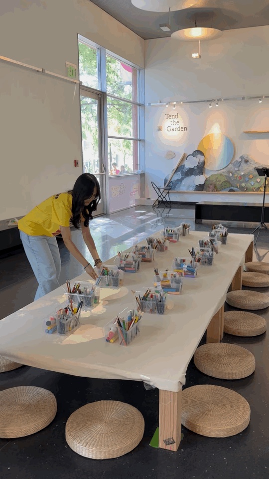 A volunteer arranges art materials around the collaborative canvas before Opening Day.