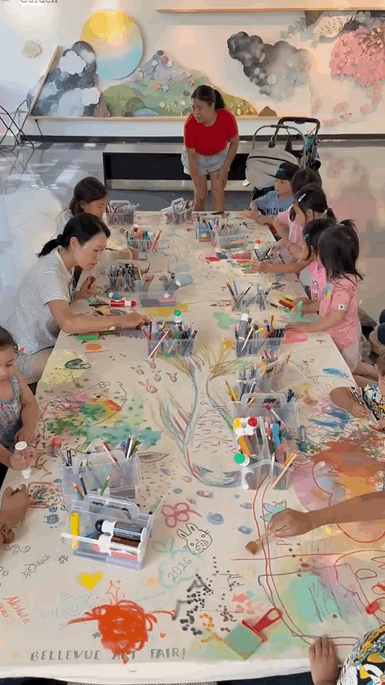 Children and caregivers gather around the collaborative canvas and make marks together.