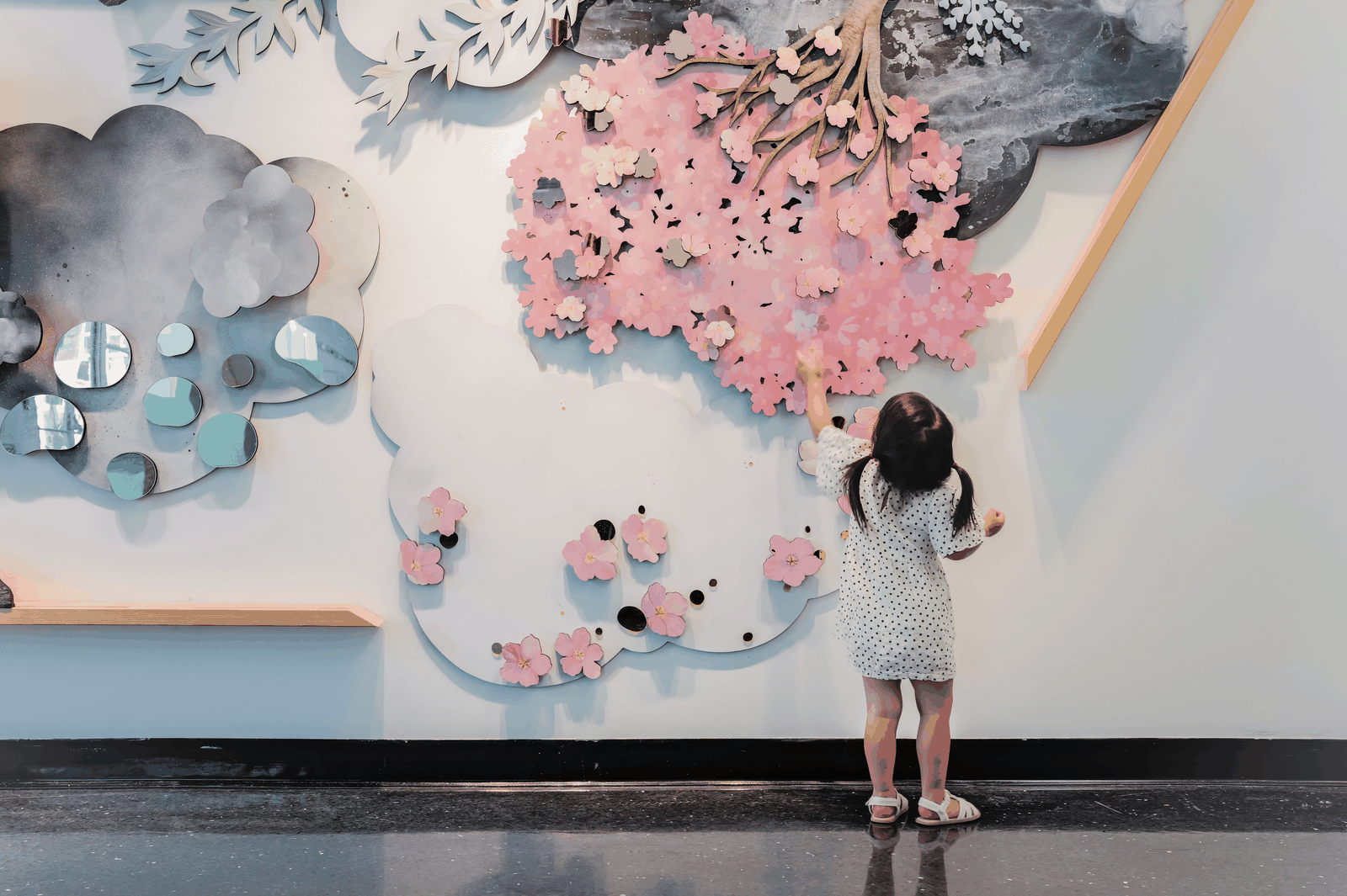 A young child reaches into the layered pink blossoms of the interactive cherry blossom garden.