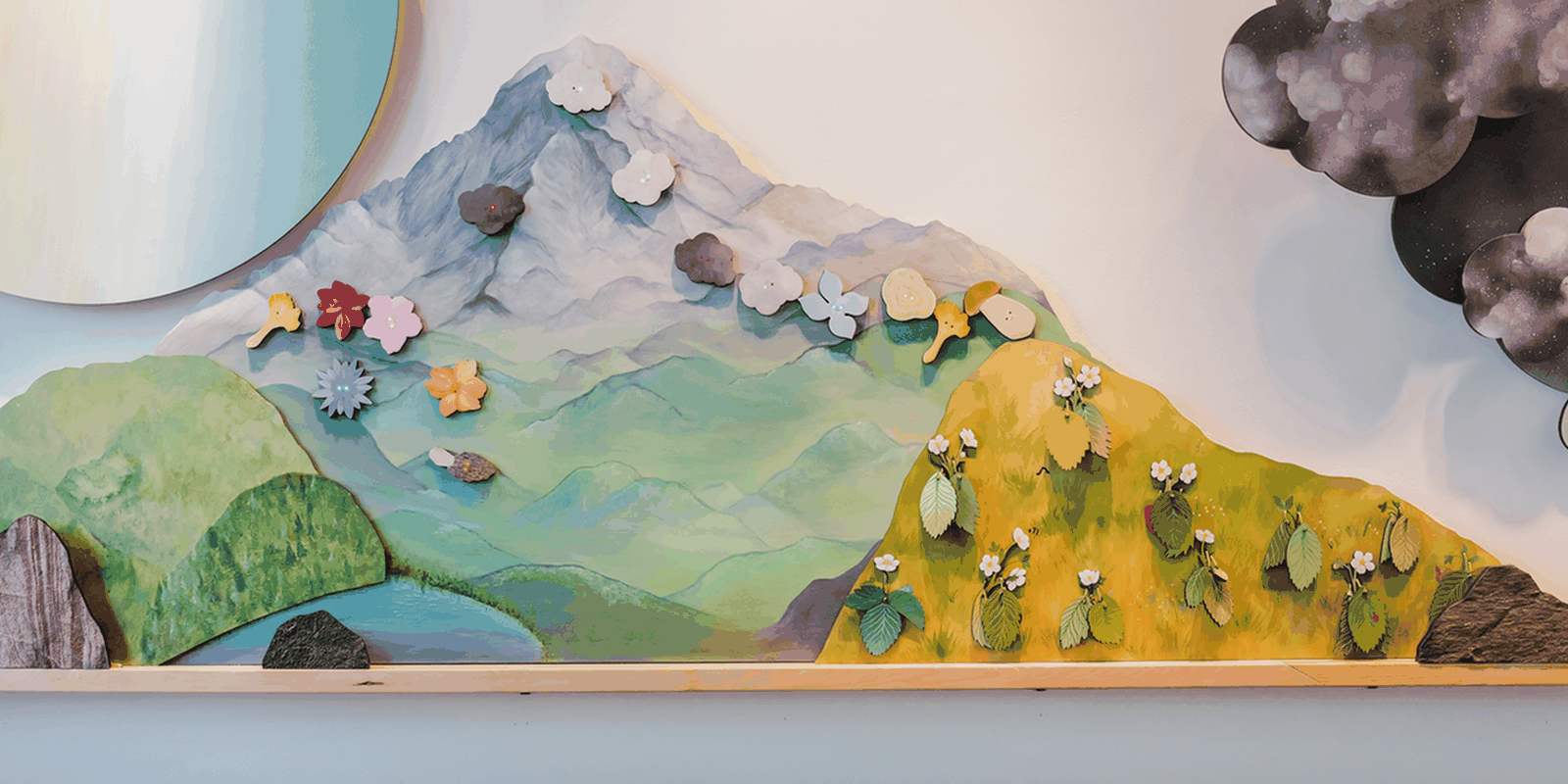 Flowers, mushrooms, clouds, and other magnetic elements continually rearrange across the painted mountain meadow.