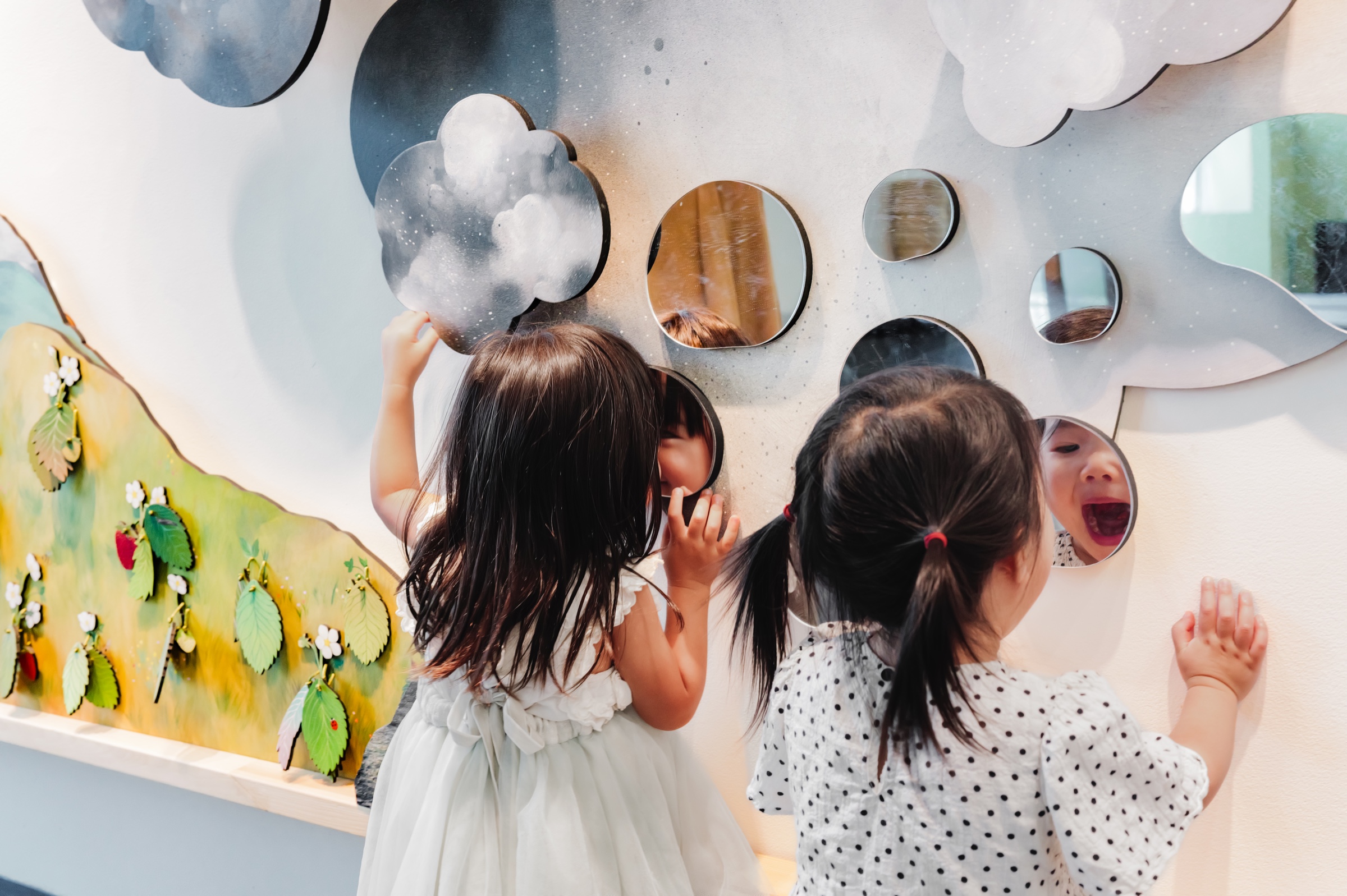 Two children discover their reflections in the mirror-acrylic raindrops of Tend the Garden.