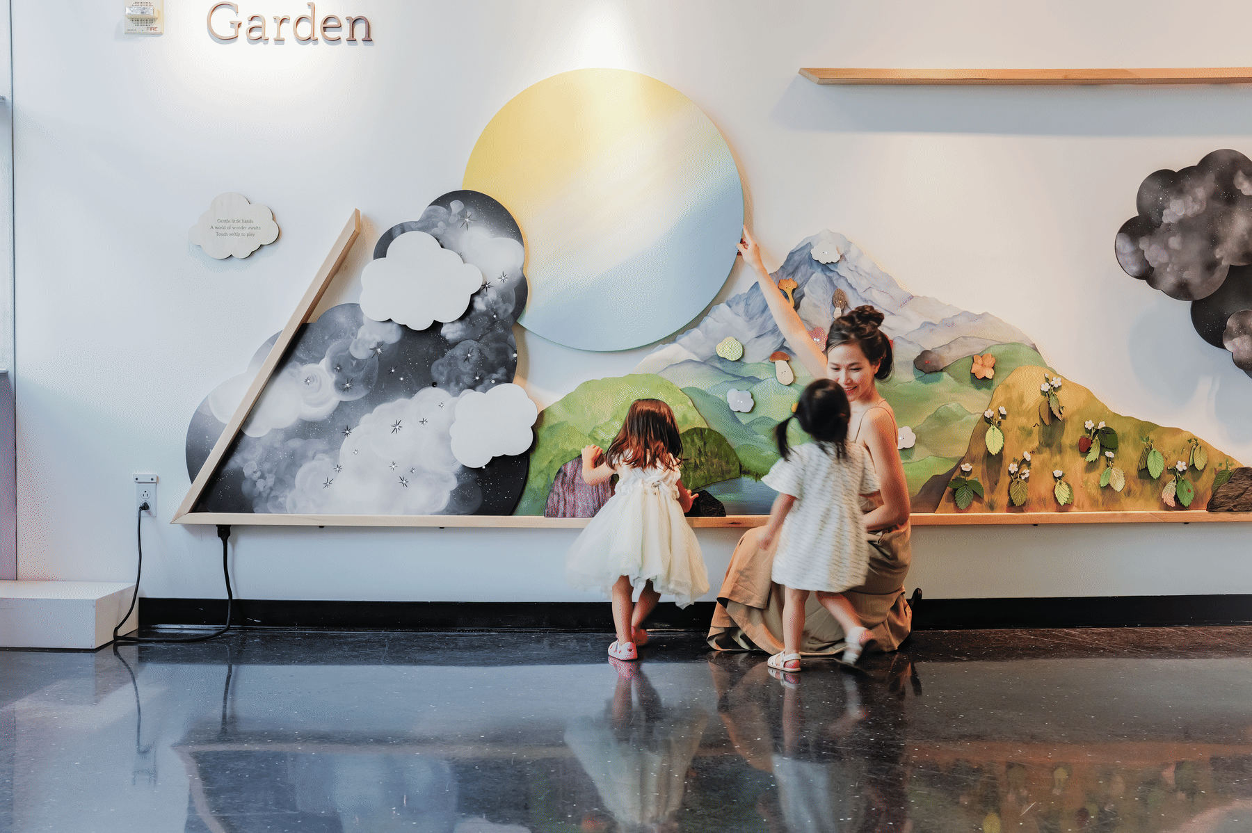 Two children and a caregiver turn the large painted sun in Tend the Garden.